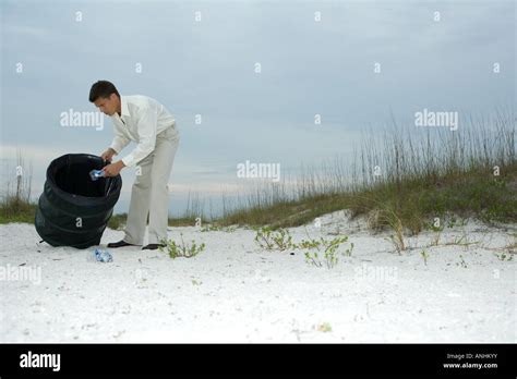 Man Digging Through Trash Can On Beach Removing Plastic Bottles Stock