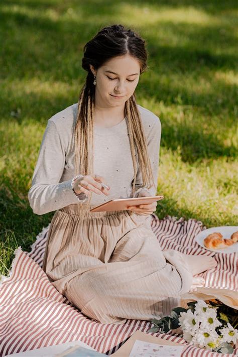 Woman In White Long Sleeve Dress Sitting On Grass Field Holding An Ipad