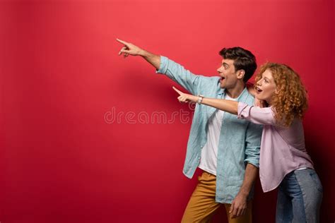 Excited Couple In Casual Clothes Pointing Isolated On Red Stock Image