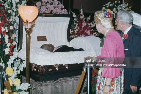 View Of Mourners Standing In Front Of The Open Casket Containing The