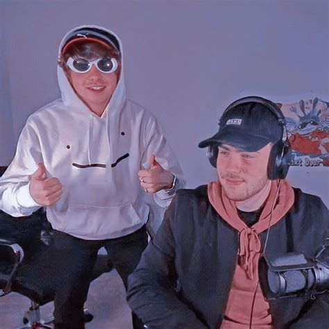 Two Men Wearing Headphones And Hoodies Sitting Next To Each Other In