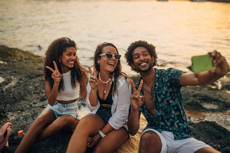 A Multiracial Group Of Friends Take Selfies While Sitting On The