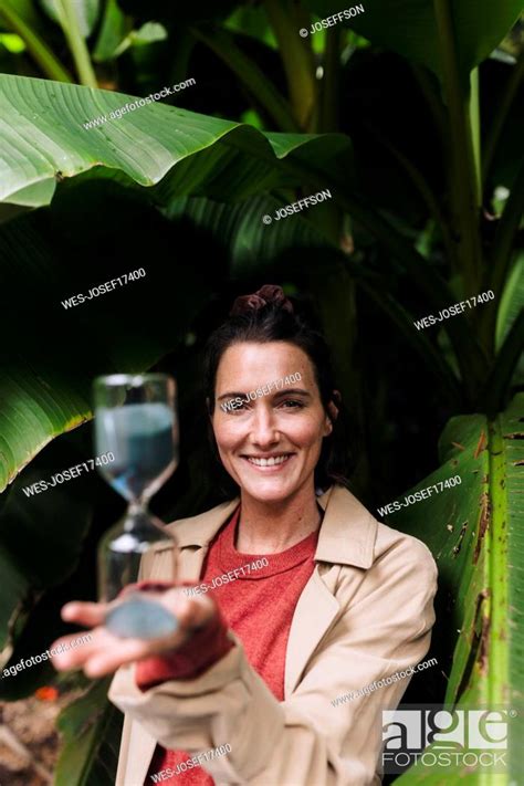 Happy Woman With Hourglass Standing In Front Of Banana Tree Stock