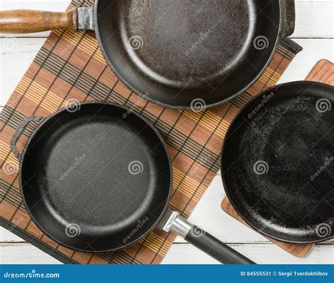 Several Empty Cast Iron Frying Pans On A White Wooden Background View