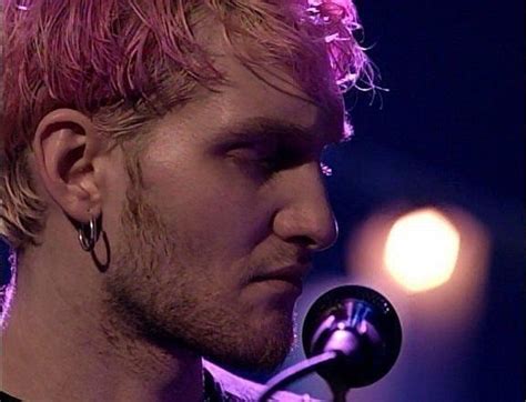 A Man With Pink Hair And Piercings On His Ear Is Singing Into A Microphone