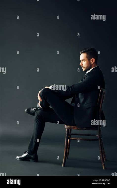 Confident Handsome Man In Black Suit Sitting On The Chair On Dark