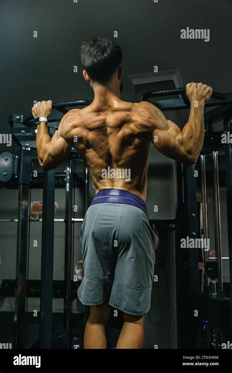 Back View Of Muscular Man Doing Pull Ups On A Bar In A Dimly Lit Gym Showcasing His Well Defined