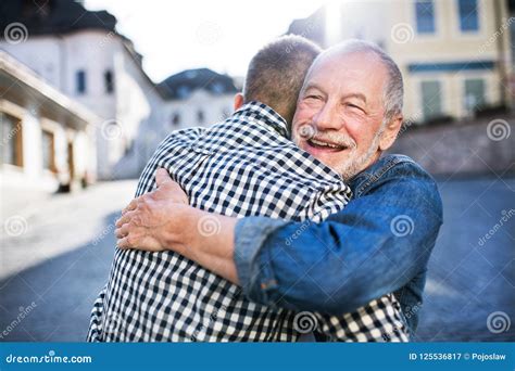 An Adult Hipster Son And His Senior Father In Town Hugging Stock