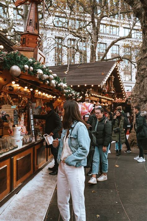 A Woman Standing In Front Of A Christmas Market With Lots Of People