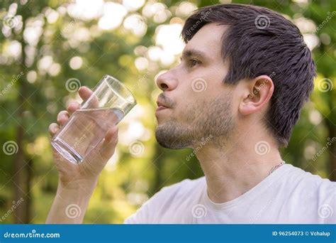 Young Man Is Drinking Water From Glass In Nature At Sunny Hot Day Stock