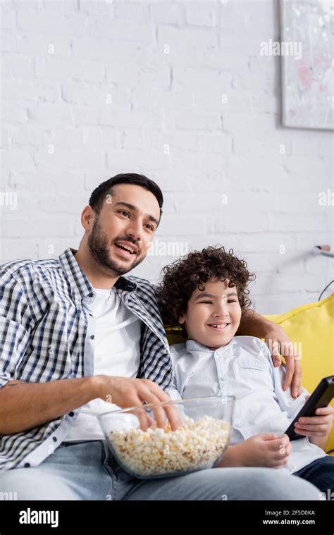 Cheerful Muslim Father And Son Watching Tv Near Popcorn At Home Stock