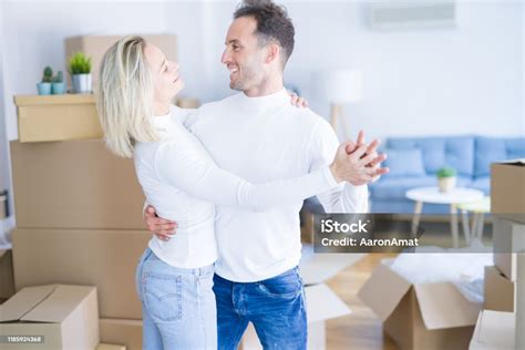 Young Beautiful Couple Dancing At New Home Around Cardboard Boxes Stock