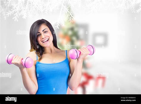 Smiling Fit Brunette Holding Dumbbells Against Blurry Christmas Tree In