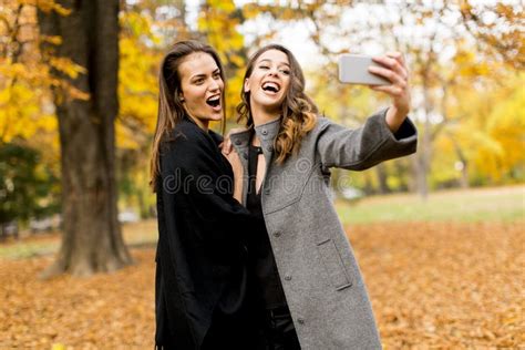 Two Young Women Taking Selfie With Mobile Phone In The Autumn Pa Stock