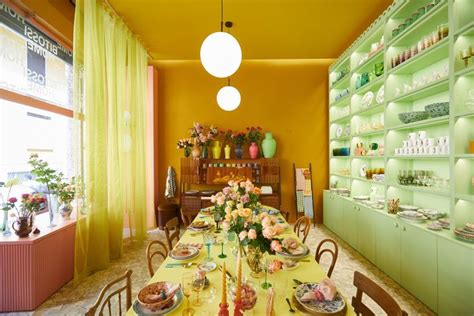 A Long Table With Plates And Flowers On It In Front Of Green Shelves