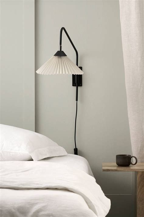 A Lamp That Is On The Side Of A Wall Next To A Bed With White Sheets