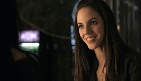 A Woman With Long Dark Hair Smiling At The Camera In A Dimly Lit Room