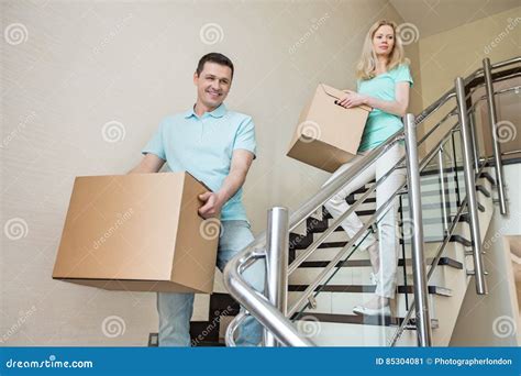 Couple Carrying Cardboard Boxes While Moving Down Steps At New Home