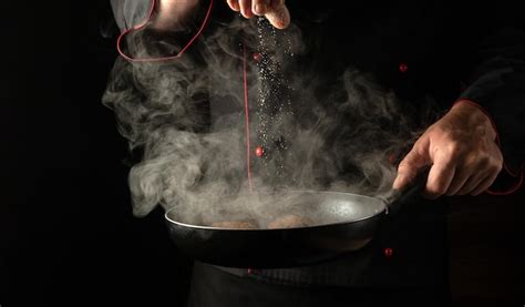 Premium Photo Adding Salt To Meat Steaks In A Hot Pan With Steam In The Hands Of A