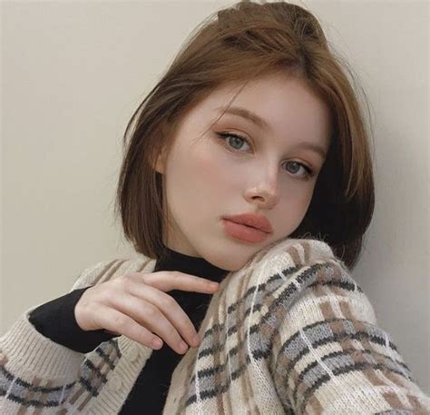 A Young Woman Poses In Front Of A White Wall With Her Hand On Her Shoulder