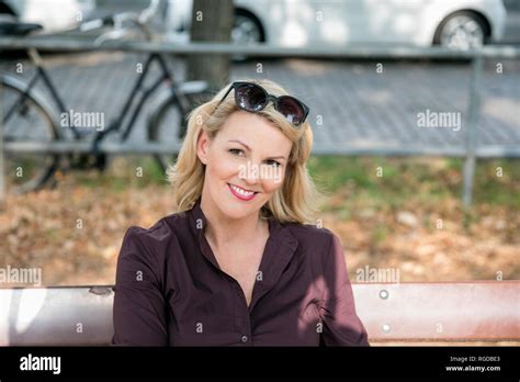 Portrait Of Smiling Blond Mature Woman Sitting On Bench Outdoors Stock Photo Alamy