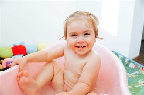 Mirando A La Cámara Una Niña Sentada En El Baño Levanta Una Pierna Sostiene La Bañera Sonríe