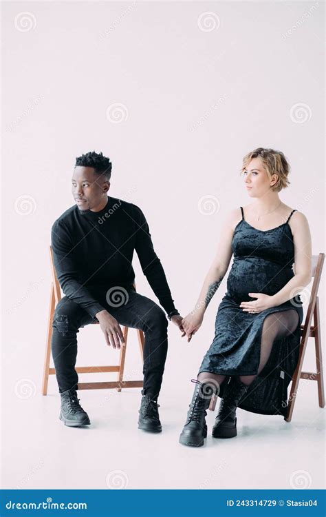 Young African Man And His Caucasian Pregnant Woman Sit On Chairs Stock