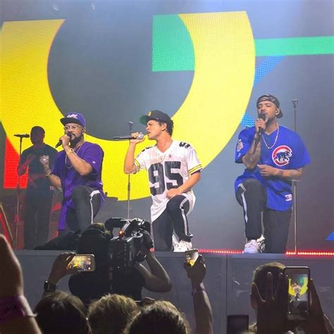 Two Men On Stage Singing Into Microphones While People Take Pictures