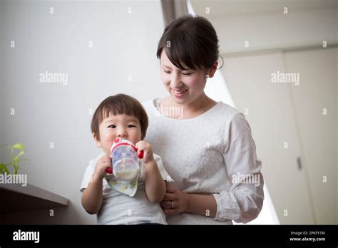 Baby Sitting On Mothers Lap Drinking Milk From A Mug Stock Photo Alamy