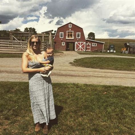 A Woman Holding A Baby Standing In Front Of A Barn