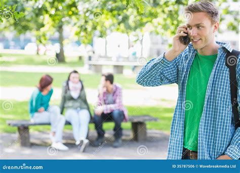 College Boy Using Cellphone With Blurred Students In Park Stock Photo