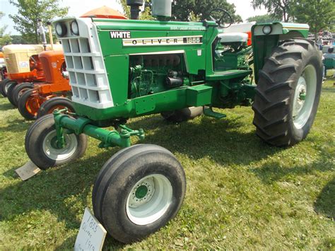 An Old Green Tractor Parked On Top Of A Lush Green Field Next To Other