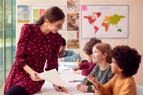 Maestra De Escuela Primaria Femenina Sonriente Trabajando En Un Escritorio En El Aula Con