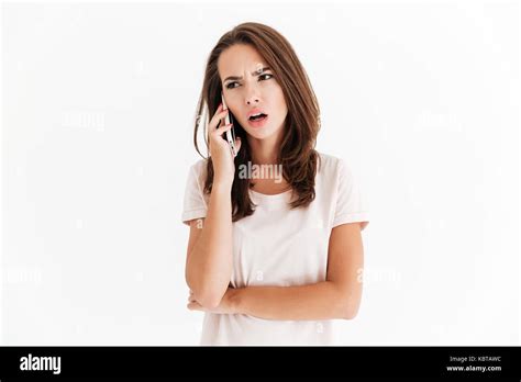 Confused Brunette Woman Talking By The Smartphone Over White Background