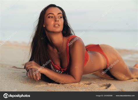 Beautiful Tanned Brunette Girl In Red Swimsuit Lying On Sandy Beach