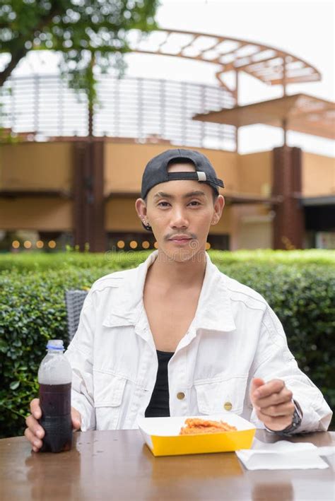 Cute Non Binary Gay Man Eating Fried Chicken And Drinking Cola Outdoors During Summer Stock