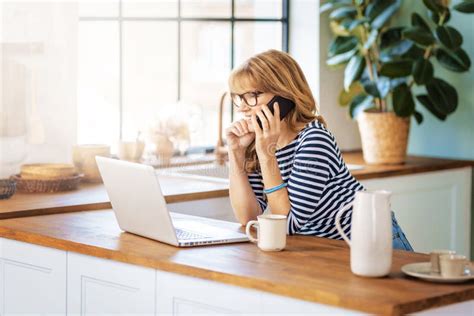 Shot Of A Mature Woman Having A Call While Relaxing In The Kitchen