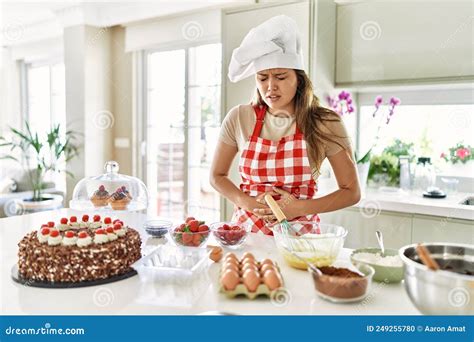 Beautiful Young Brunette Pastry Chef Woman Cooking Pastries At The Kitchen With Hand On Stomach