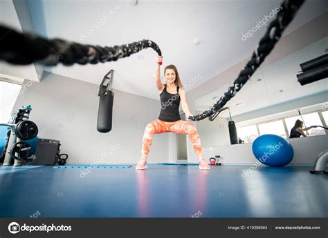 Attractive Fit Woman Squatting While Using Battling Ropes Gym Stock