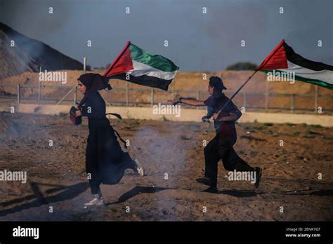 Palestinians holding flags run as Israeli forces fire tear gas canisters towards them during an ...