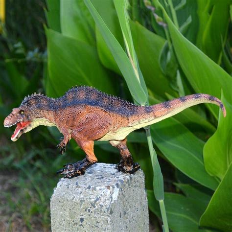 A Toy Dinosaur On Top Of A Rock In Front Of Some Green Grass And Plants