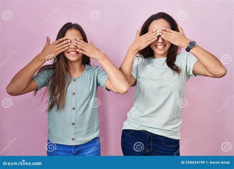 Young Mother And Daughter Standing Over Pink Background Covering Eyes