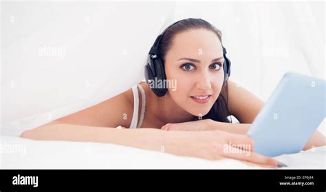 Happy Brunette Lying Under The Sheets Listening To Music Using Her