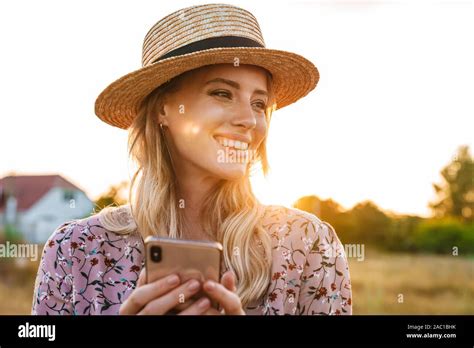 Photo Of Laughing Blonde Woman Wearing Straw Hat Using Cellphone And