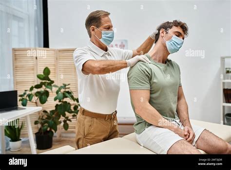 Devoted Handsome Mature Doctor In Uniform With Mask Massaging Neck Of