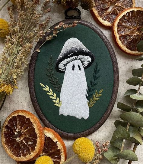 A Cross Stitch Ornament With An Image Of A Ghost Surrounded By Dried