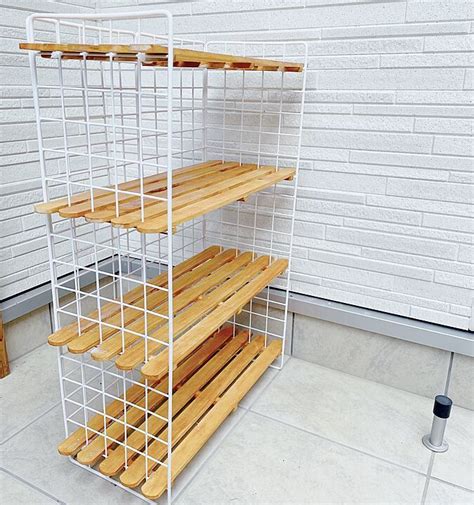 Three Tiered Shelf With Wooden Slats In Front Of A White Brick Wall And