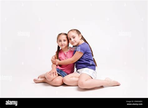 Fun Girls Sisters Sitting On The Floor On Their Knees And Hugging On