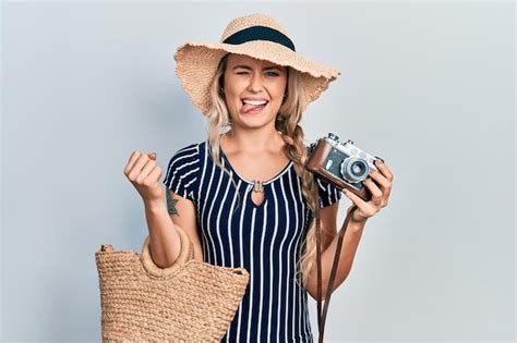 Schöne junge blonde frau mit vintage kamera zunge herausstreckt glücklich mit lustigem