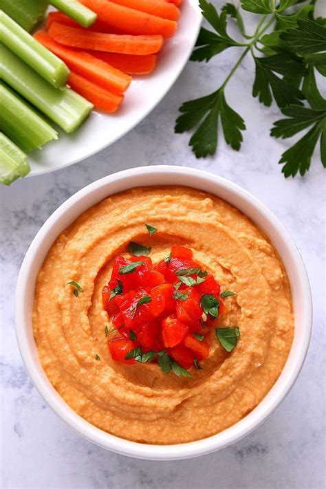 A White Bowl Filled With Hummus Carrots And Celery On A Table